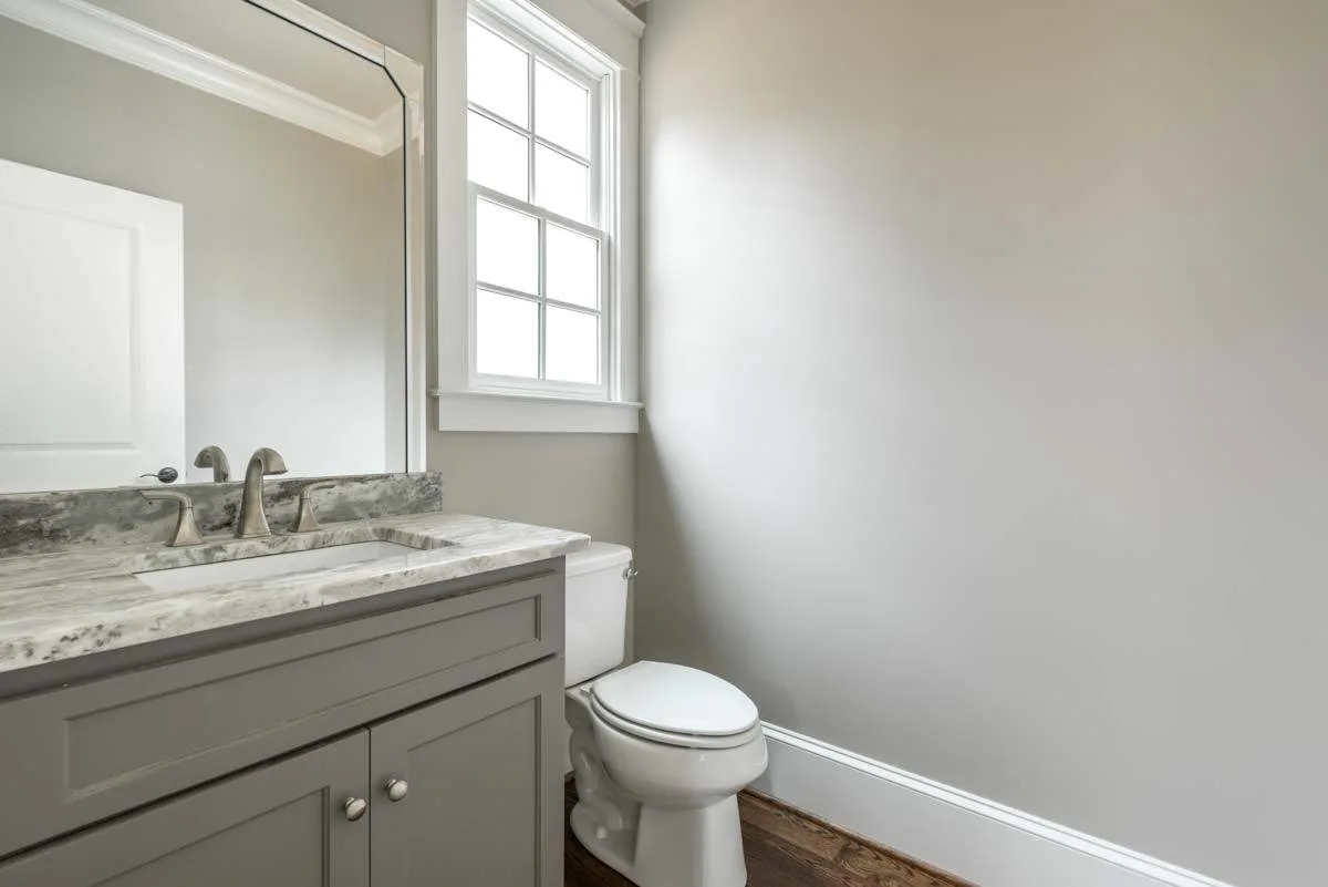 Powder room with toilet and gray marble countertop with sink.