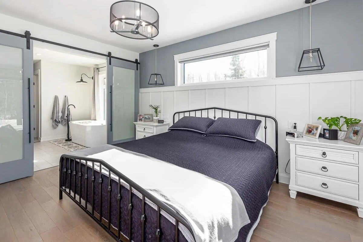 Two side tables in white frame a bed with a shiny black structure.