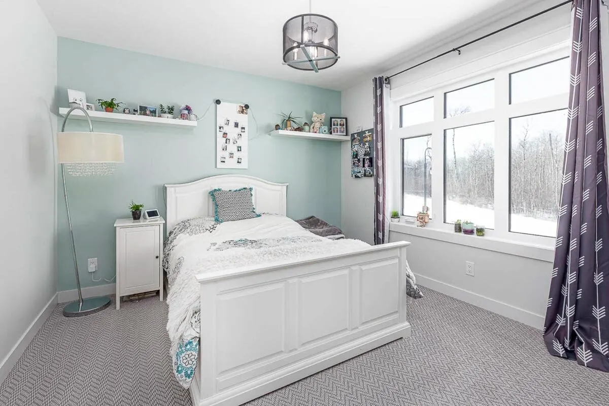 A bedroom with a green-blue wall complements the room's white furnishings and big window frames.