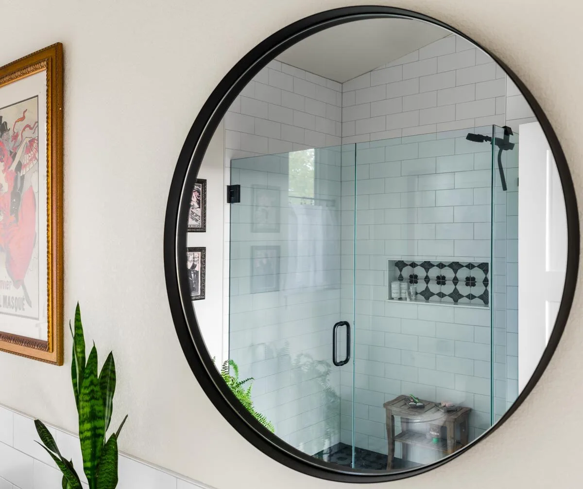 A circular black mirror frame in front of a shower in the bathroom.
