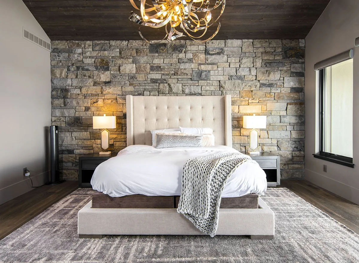 The bedroom space is designed in a sophisticated way with exposed stone wall background.