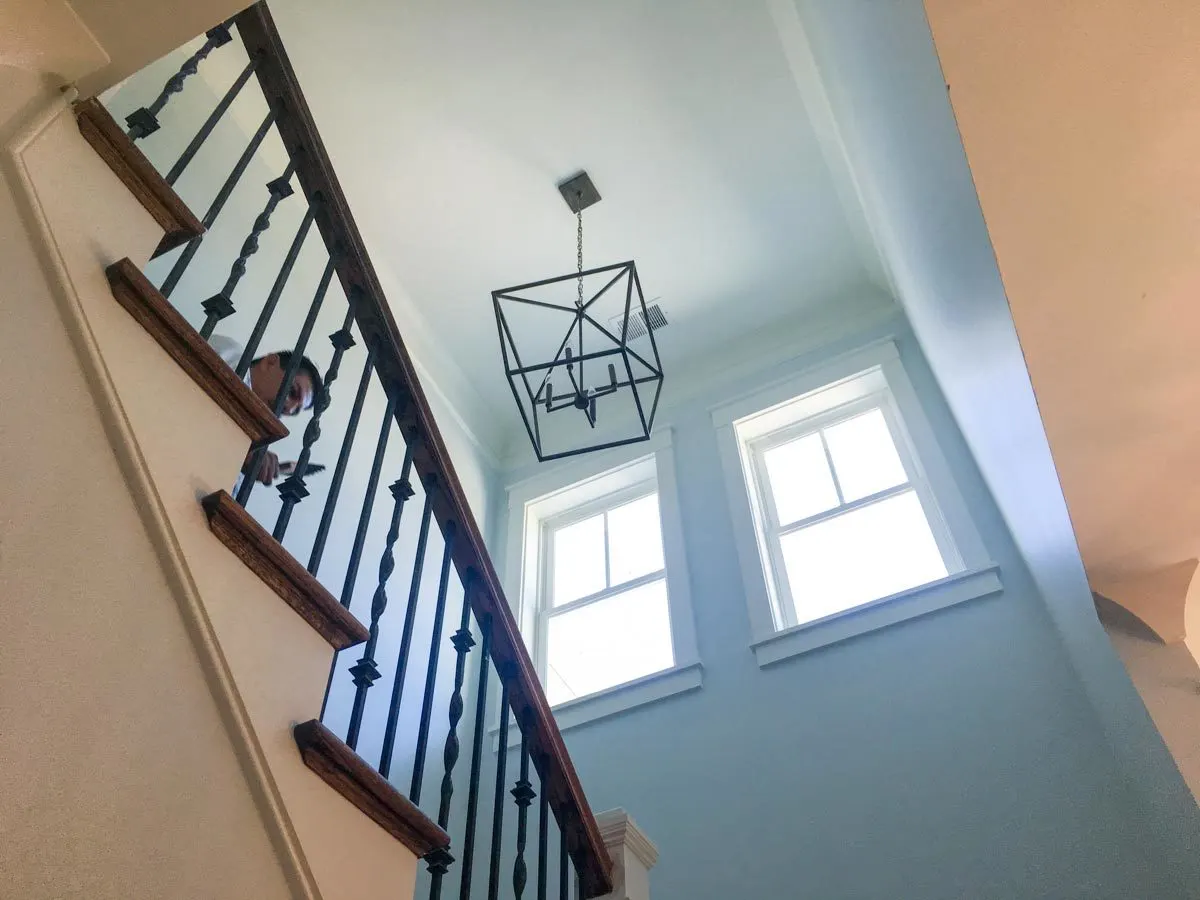 Staircase view with a geometrical lighting candle chandelier and natural light from a window.