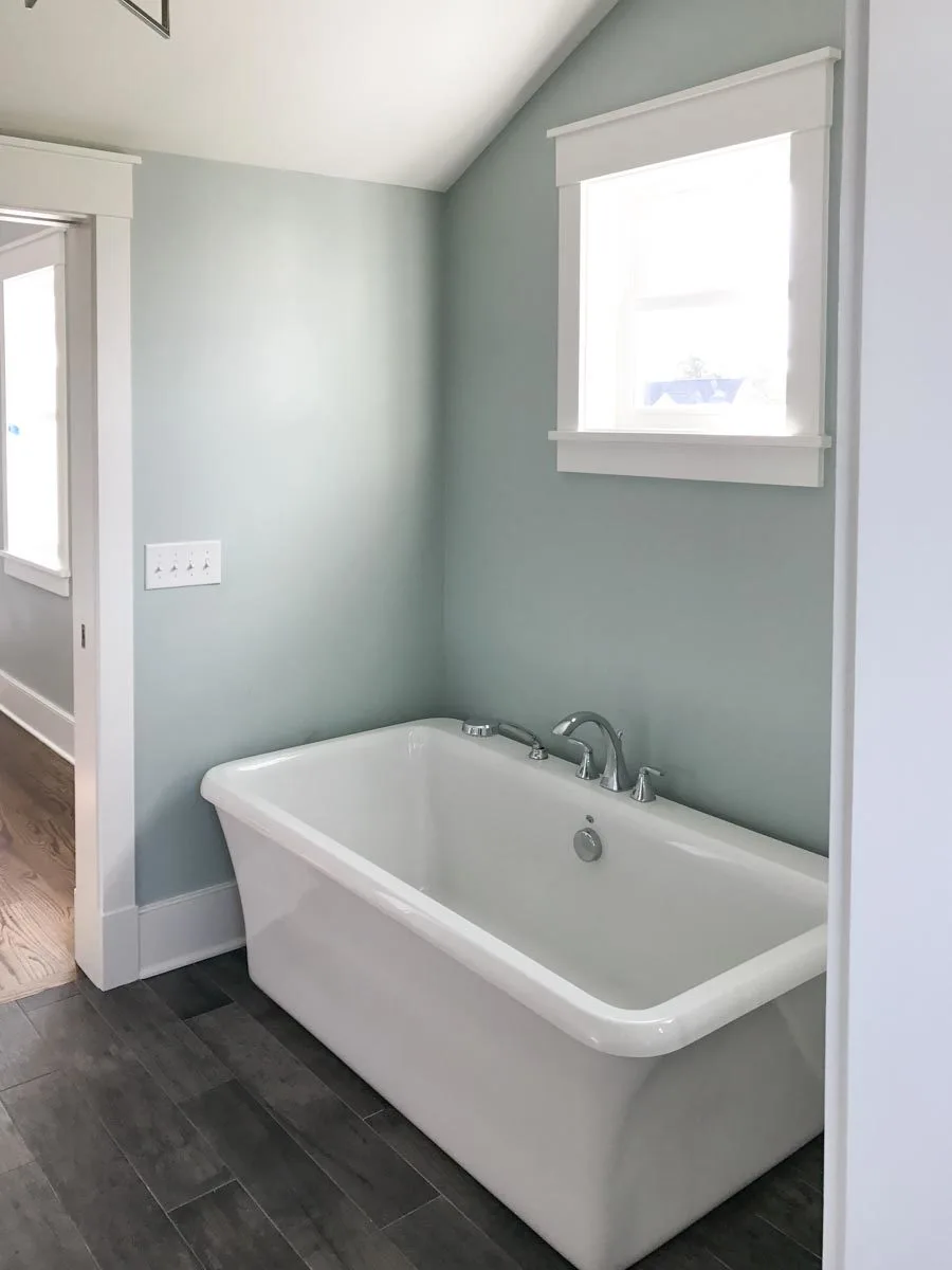 The bath tub is near the entry and a window above providing extra light in the space.