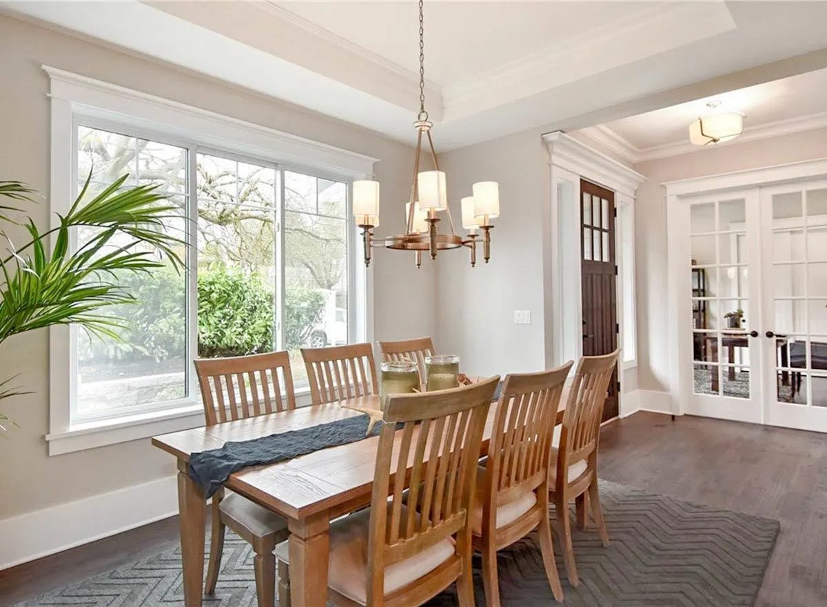 The dining area of the house with a huge glass window and an elegant low chandelier above the table.