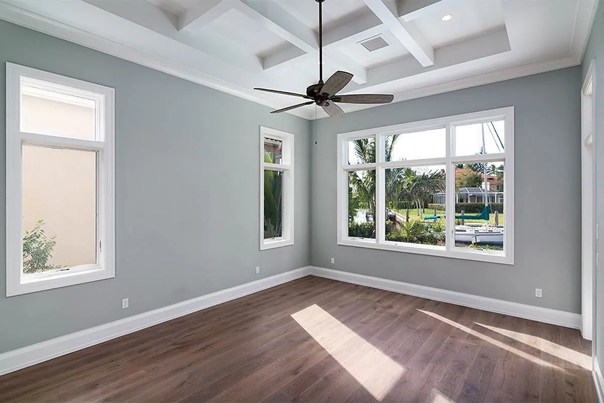 A bedroom with gray walls, white window trimmings, and a wooden floor.