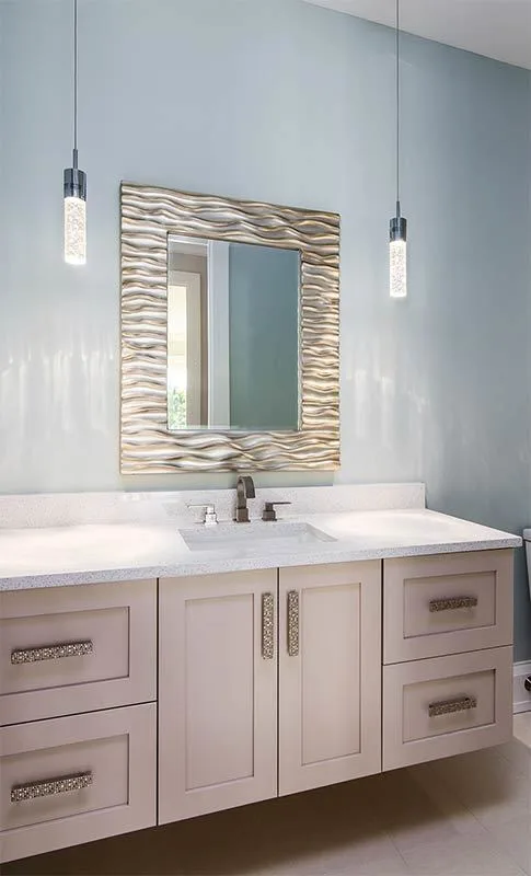 Vanity area with gleaming cabinet knobs, a wavy frame mirror, and two hanging tube lights.