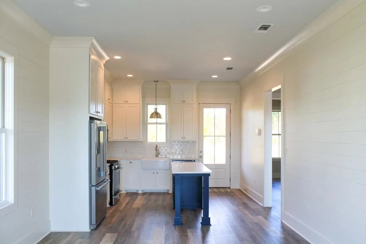 A light-filled kitchen space with a tiny island in a dark blue foundation.
