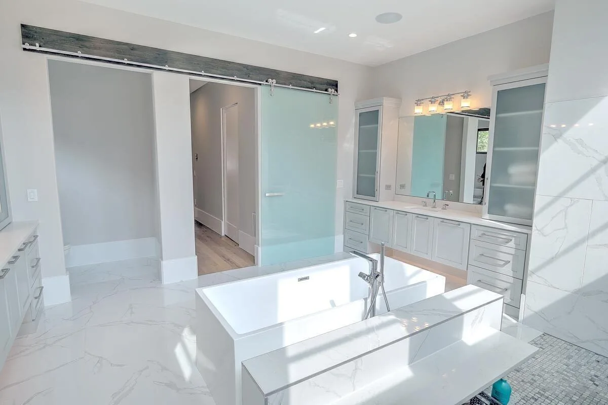 A clean white color bathtub in the middle with tiled seat on the side.