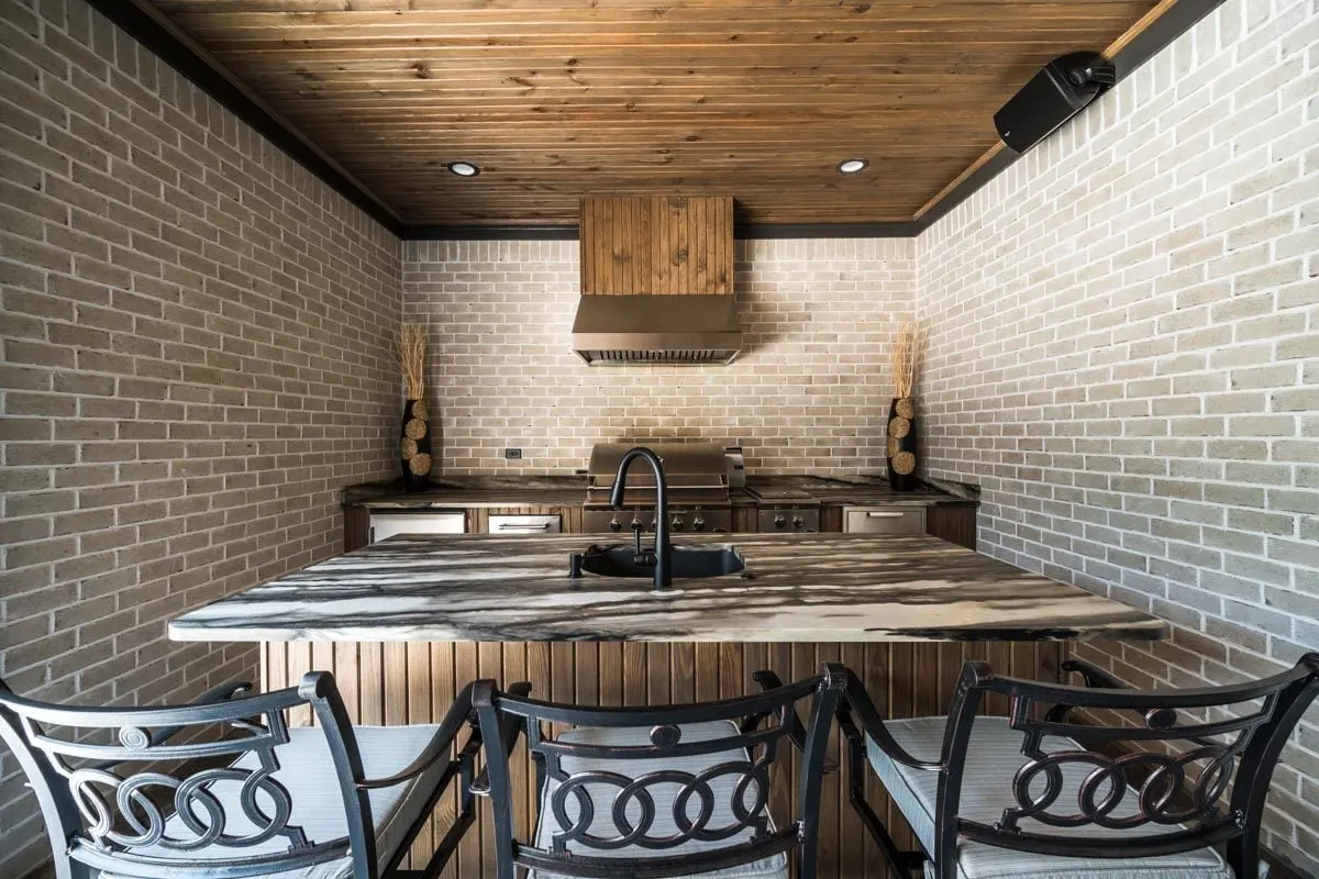 A rustic outdoor kitchen with a brick wall is featured.