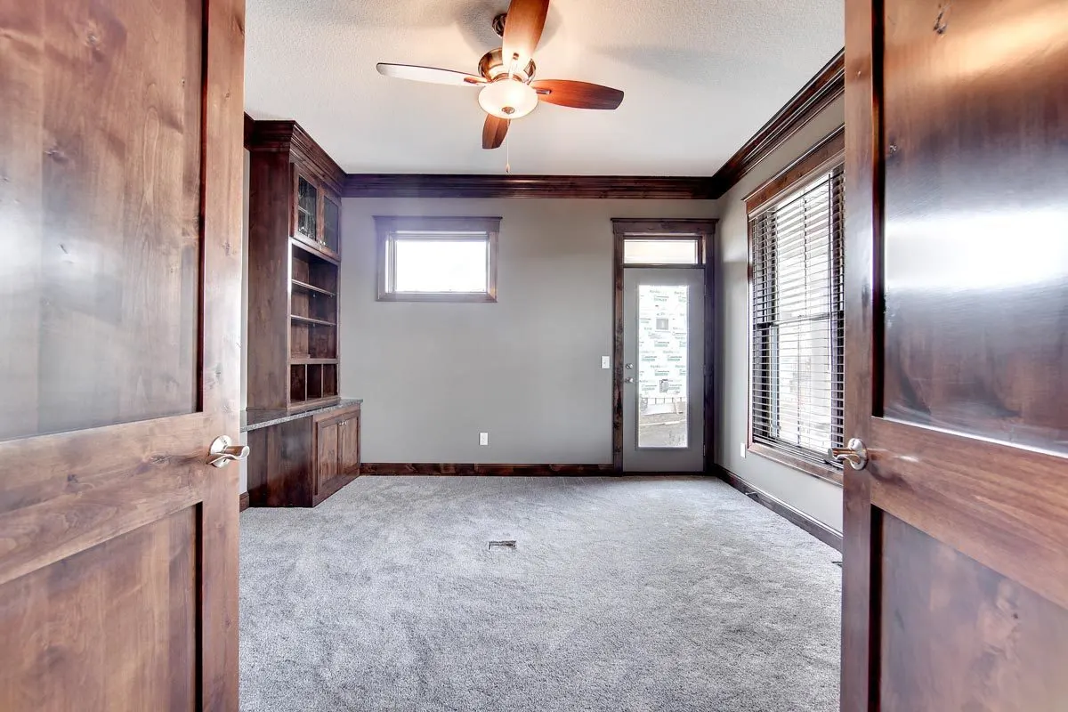 The study has a ceiling fan with a light and door access to the garage.