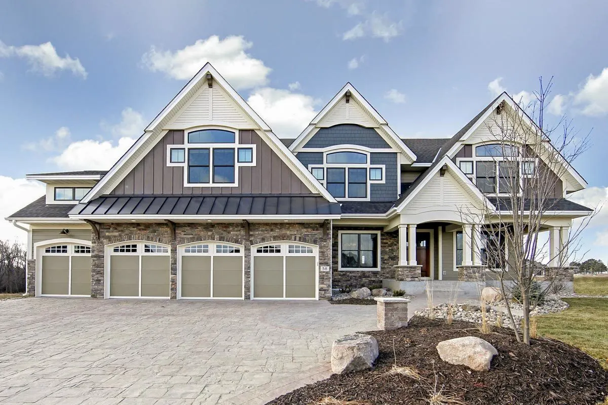 The front four-car garage door is painted in a neutral hue and has side landscaping in a dry setting.
