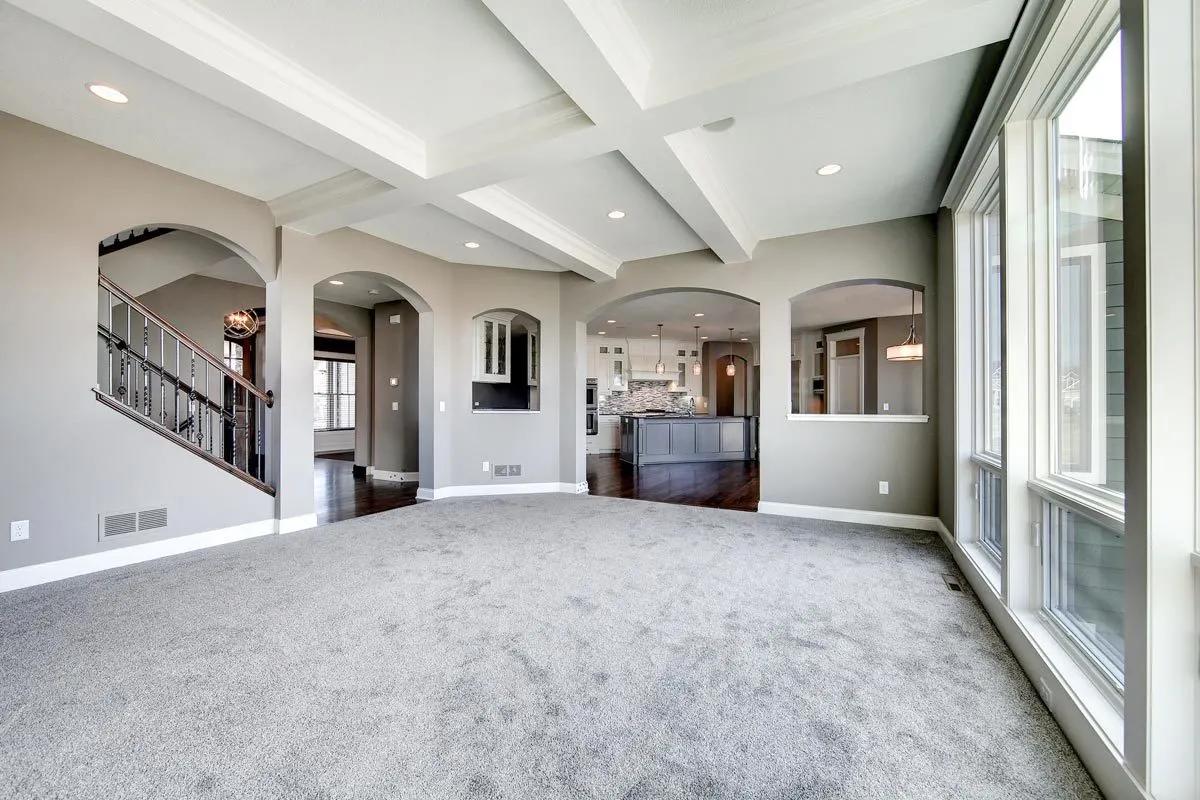 Spacious great room with gray carpeting and an arch-style entrance.