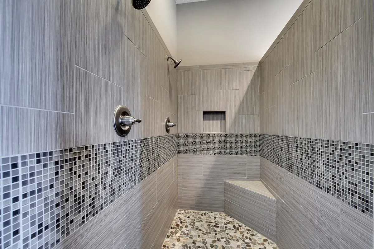 Shower area with gray interior tile pattern and two shower heads.