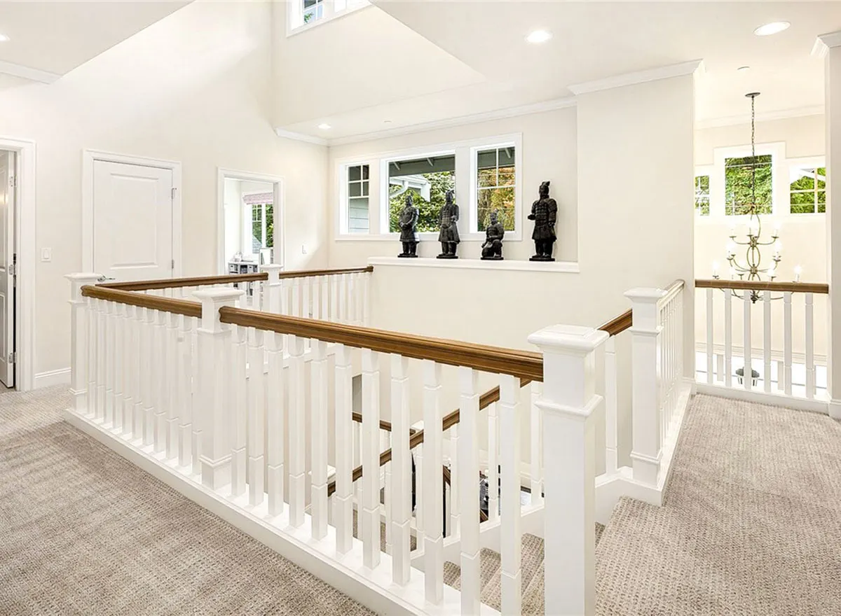 Second level hallway with wood white fence and brown handrail stairs.