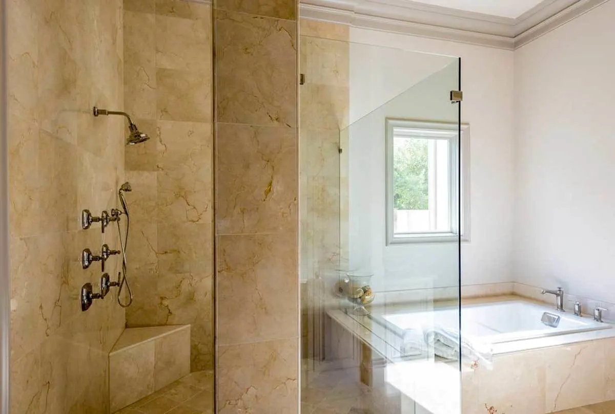 A glass-enclosed shower space with a beige tile wall.
