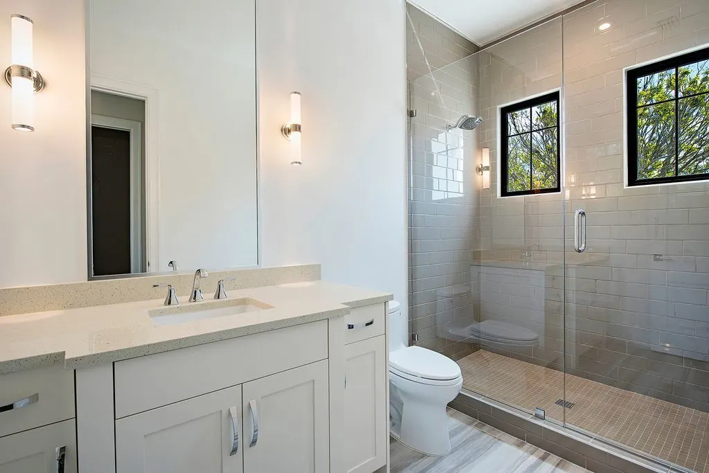 The vanity has a beige color style with a marble top and mirror, as well as side accent lights.