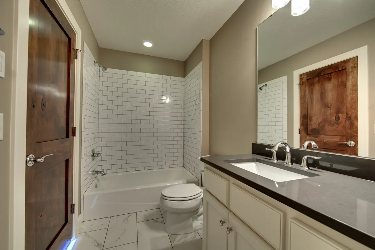 Bathroom with white tiled wall shower area with bathtub.