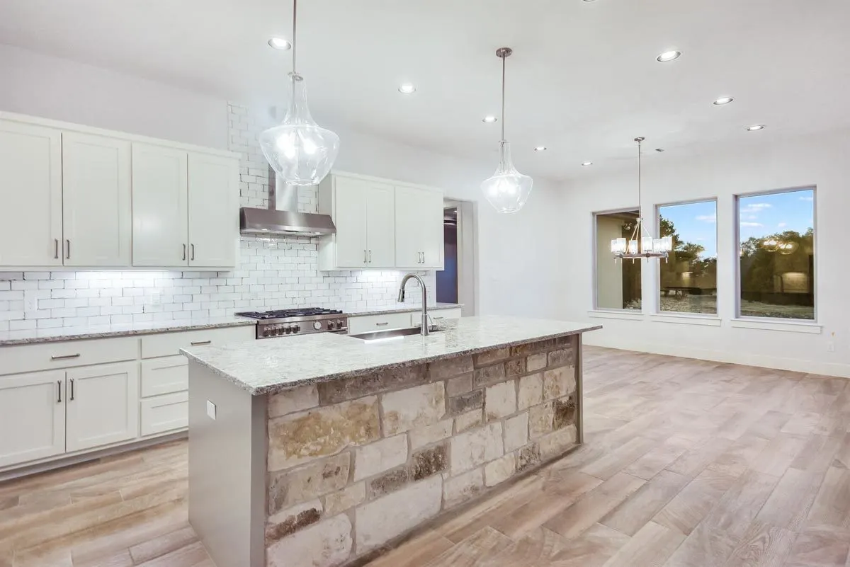 A glass chandelier hangs above a kitchen island with a stone-style foundation made of large blocks.