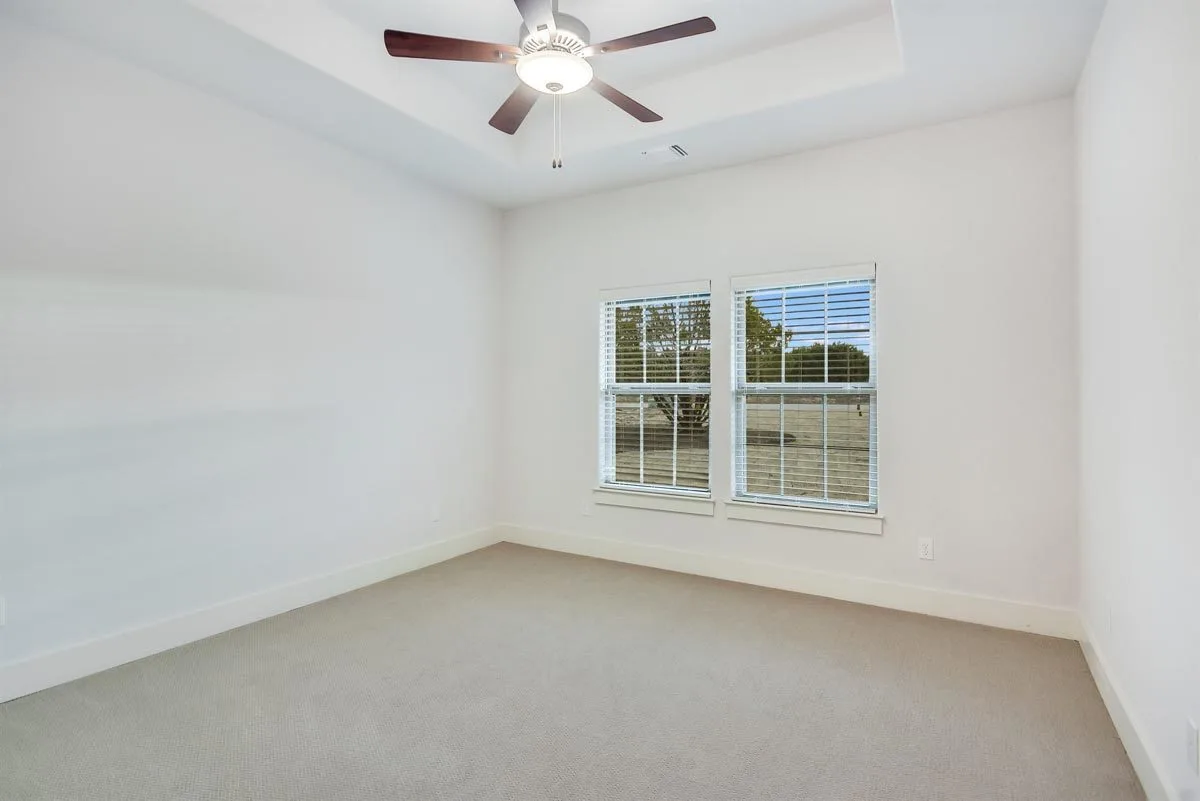 High ceiling tray-style in the bedroom area, two windows, and fan ceiling.