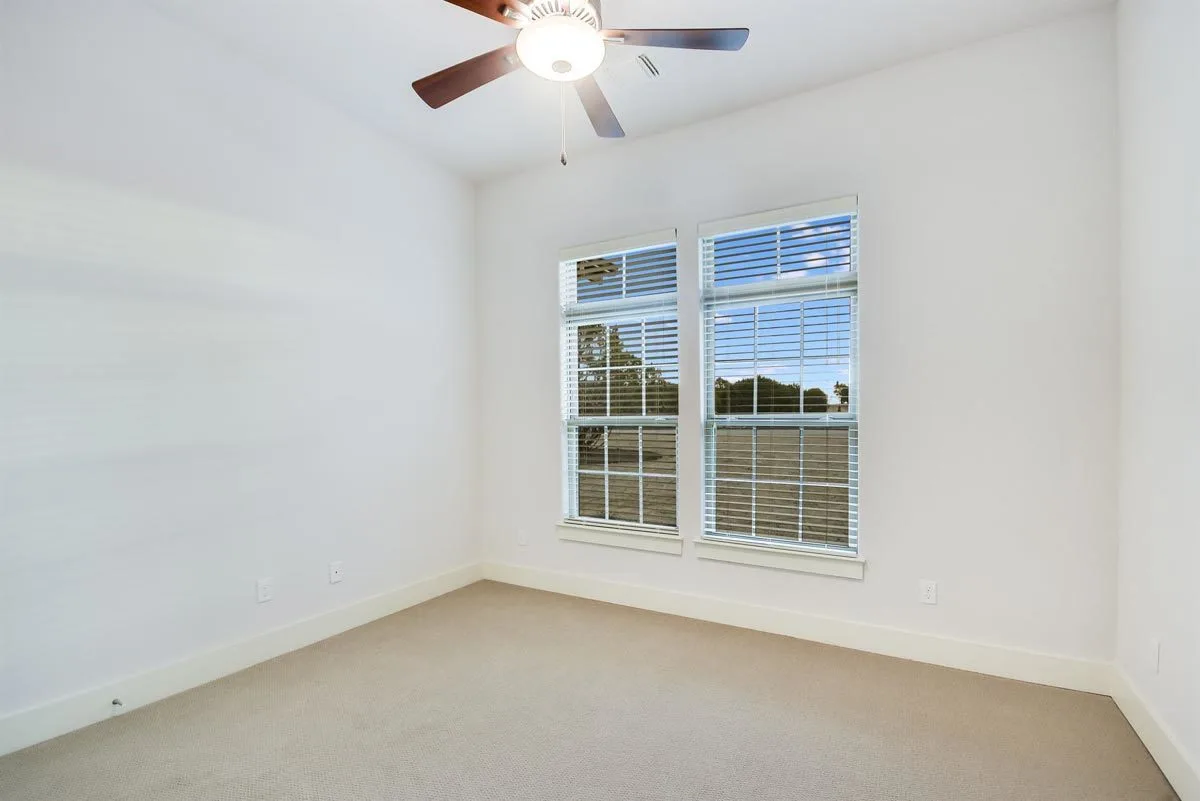 Another bedroom area with beige carpeting, white painted walls, and a window.