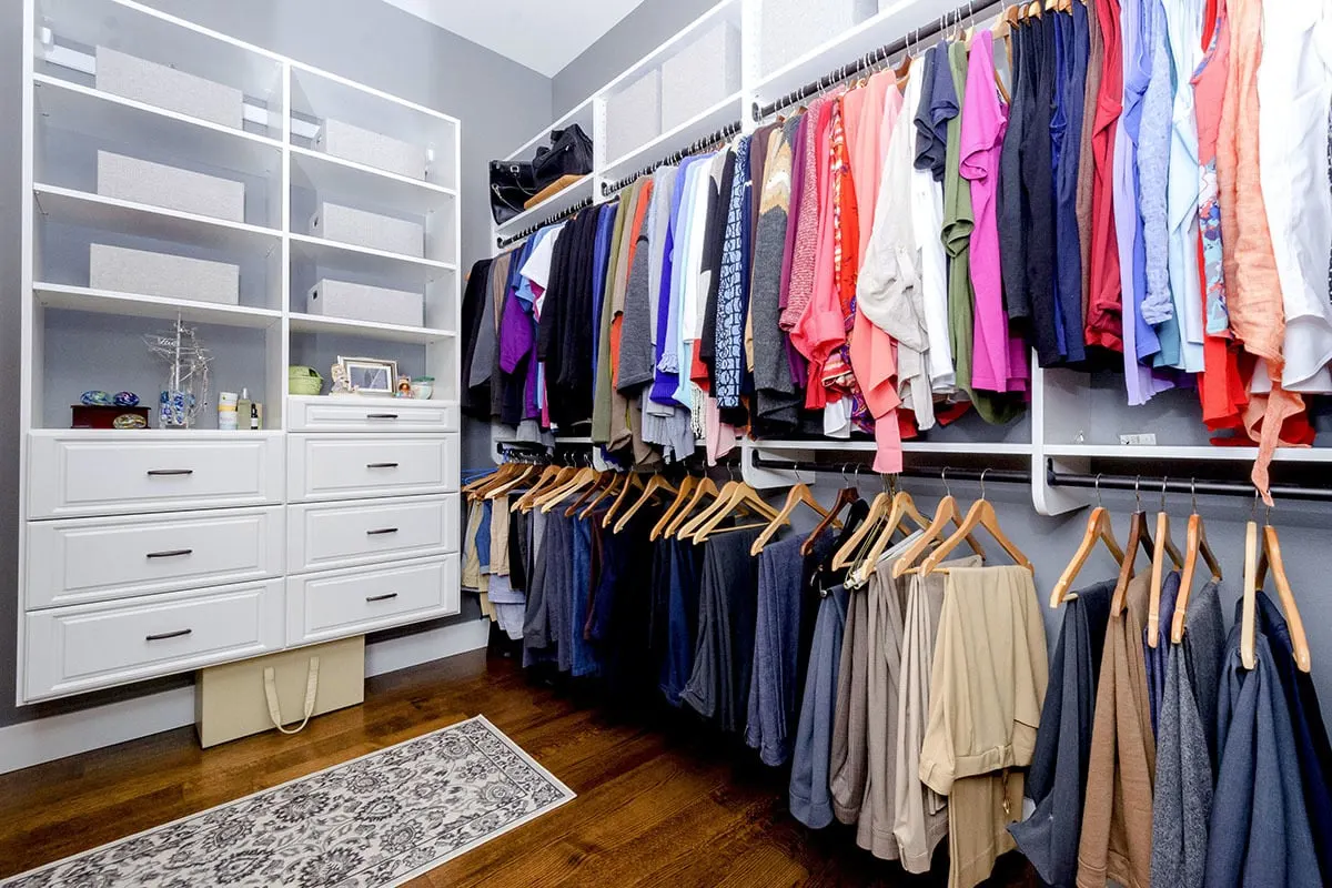 Walk-in closet with white hanging racks and drawers.
