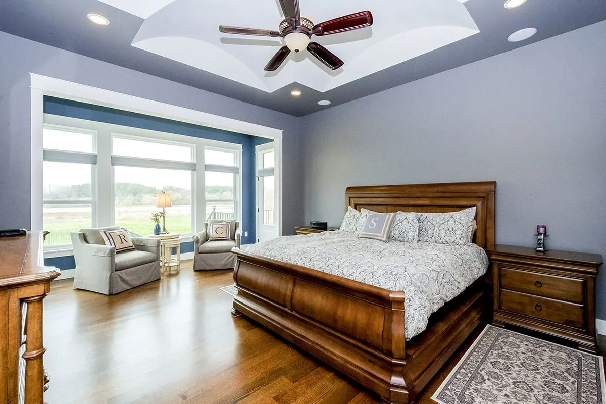 The master bedroom has a sitting area near the windows with a polished wood style floor and furniture.